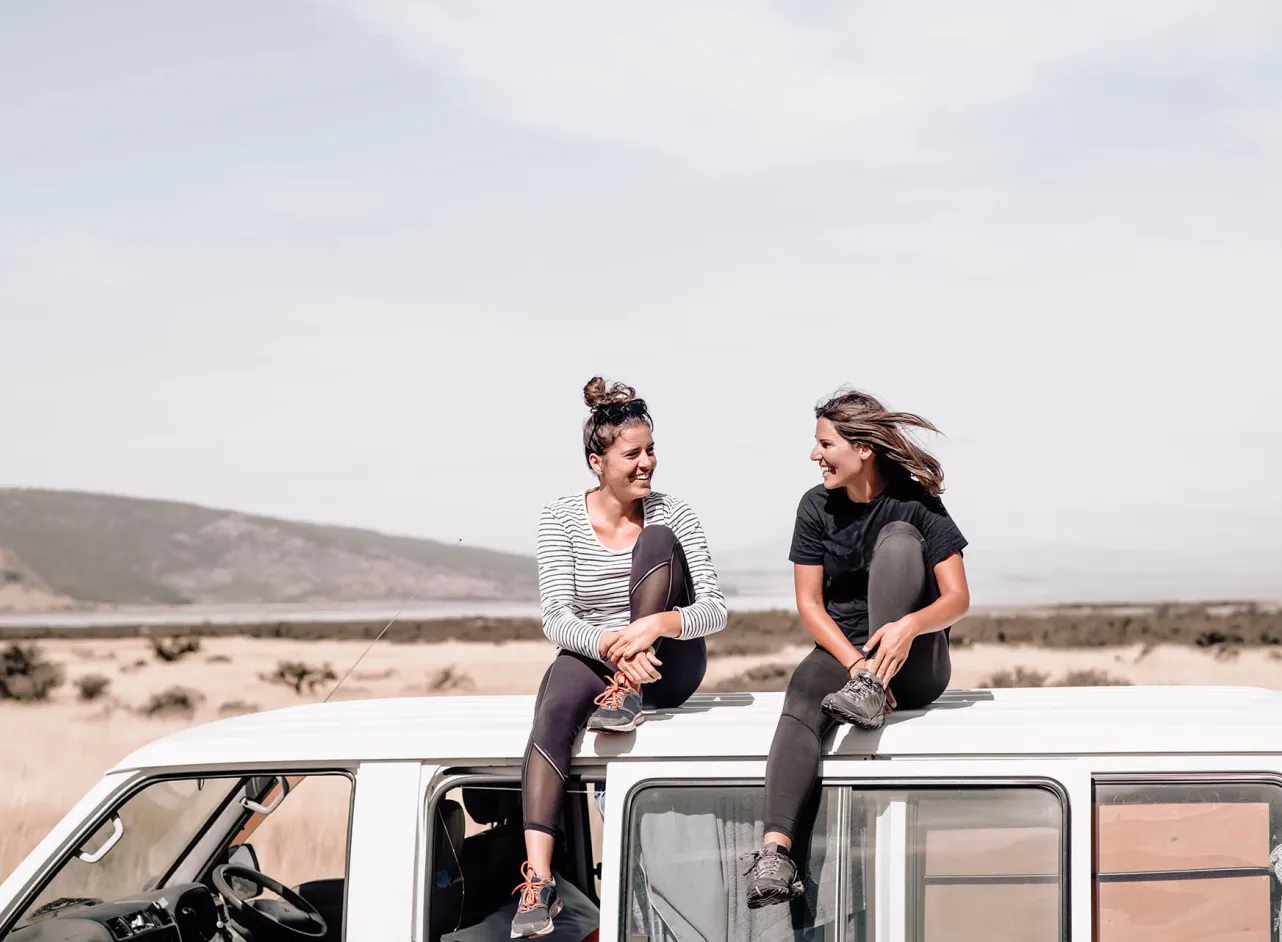 two smiling women sitting on bus roof 