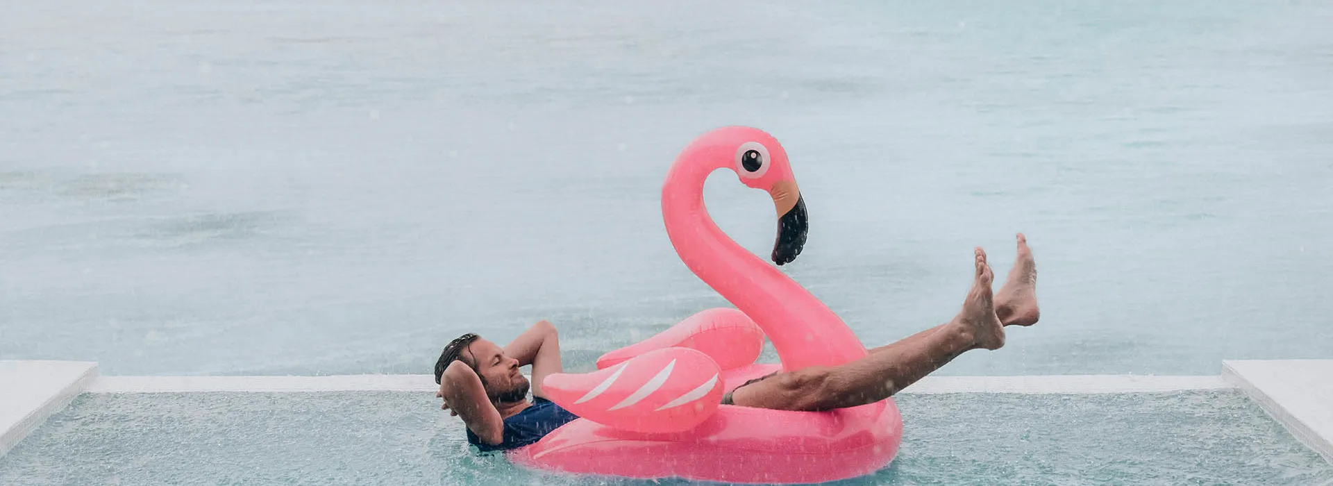 man relaxing in pool flamingo in the rain 