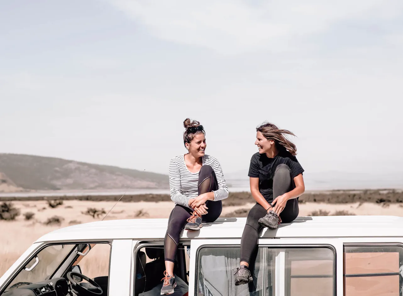 two smiling women sitting on bus roof